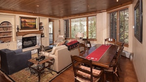 A spacious living room with a fireplace, a dining table with chairs, a sofa, and a bookshelf.