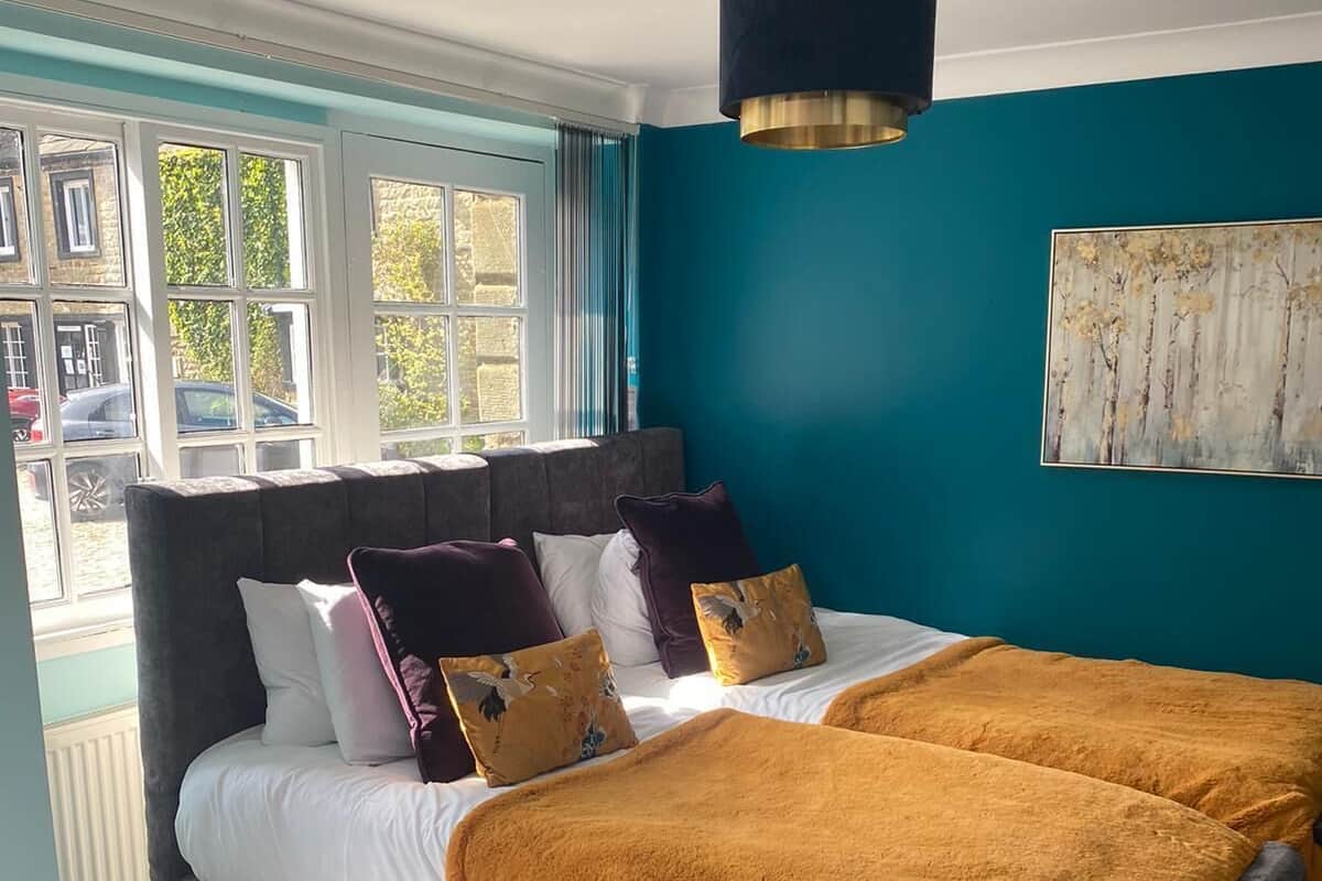 A bedroom with a large bed, a bedside table, a window with curtains, and a painting on the wall.