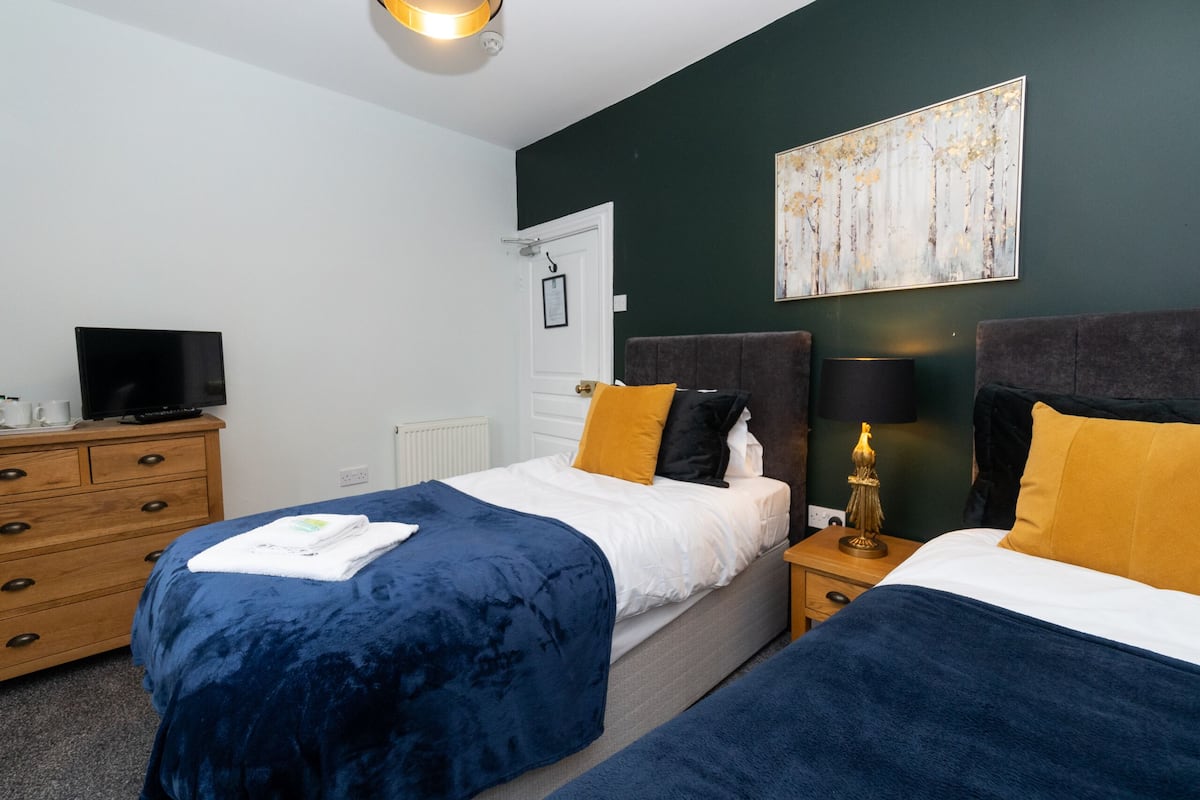 A hotel room with two beds, a dresser, a television, and a painting on the wall.