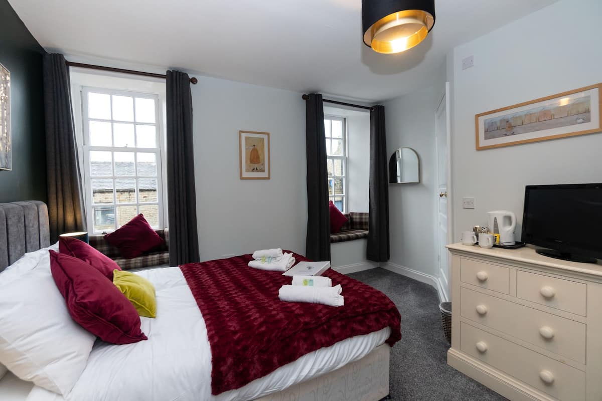A hotel room with a large bed, a television, a dresser, and a window with curtains.