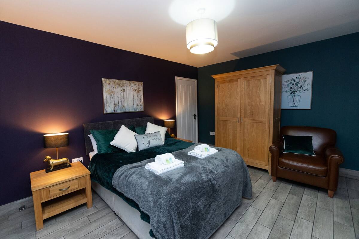 A bedroom with a bed, nightstand, chair, wardrobe, and artwork on the walls.