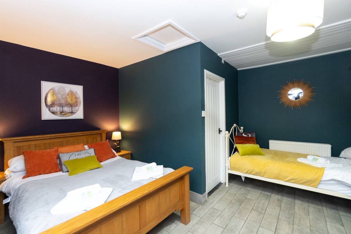 A bedroom with two beds, a wooden headboard, a nightstand, a wall-mounted mirror, and a ceiling light fixture.