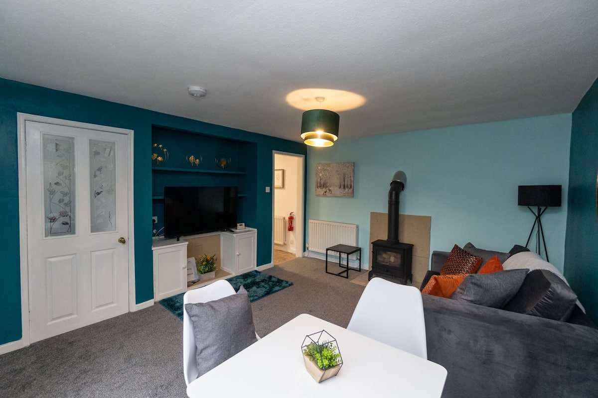A living room with teal walls, a white door, a fireplace, a TV, and a dining area with a table and chairs.