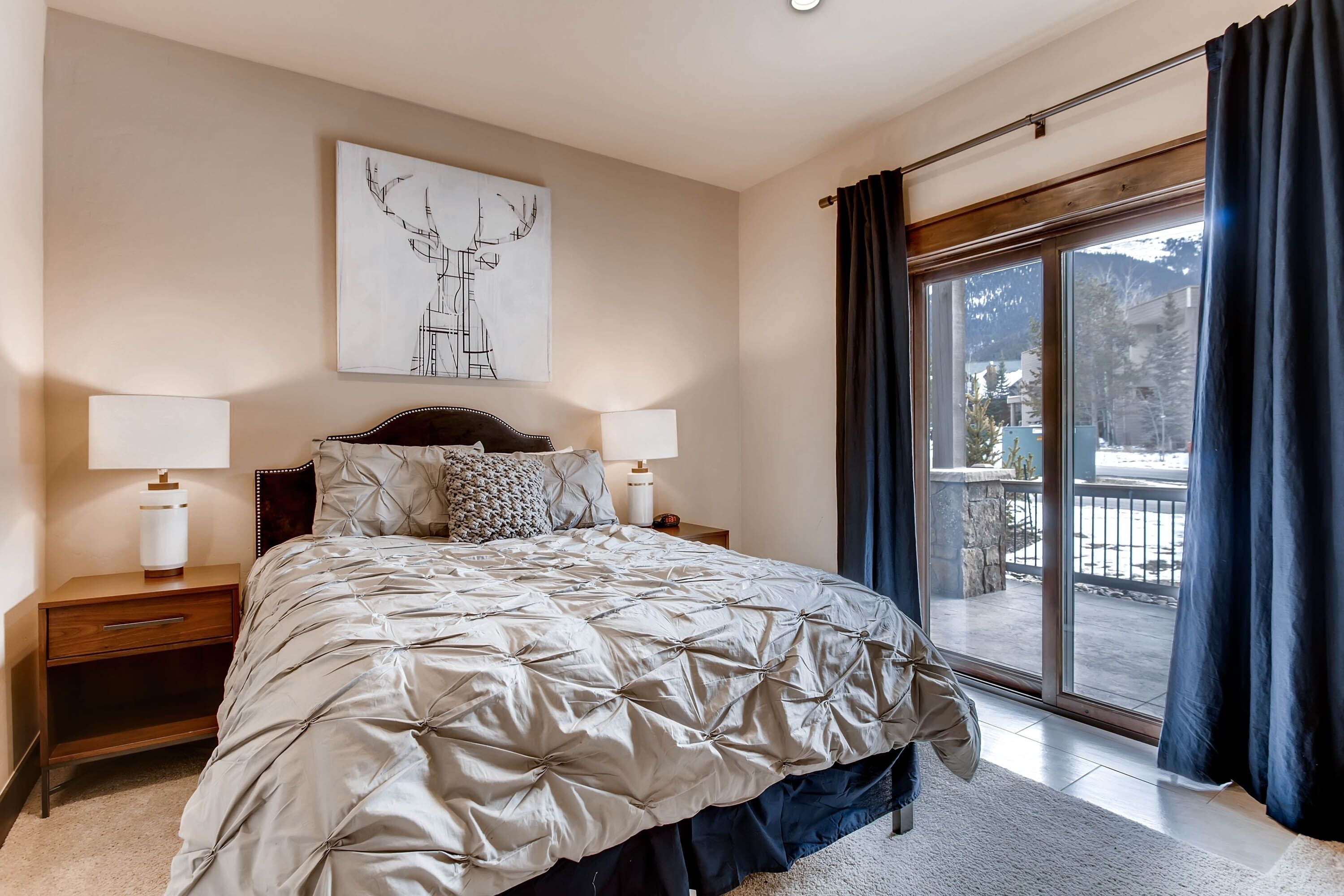 A bedroom with a large bed, two bedside tables, a wall-mounted artwork, and a sliding glass door to a balcony.