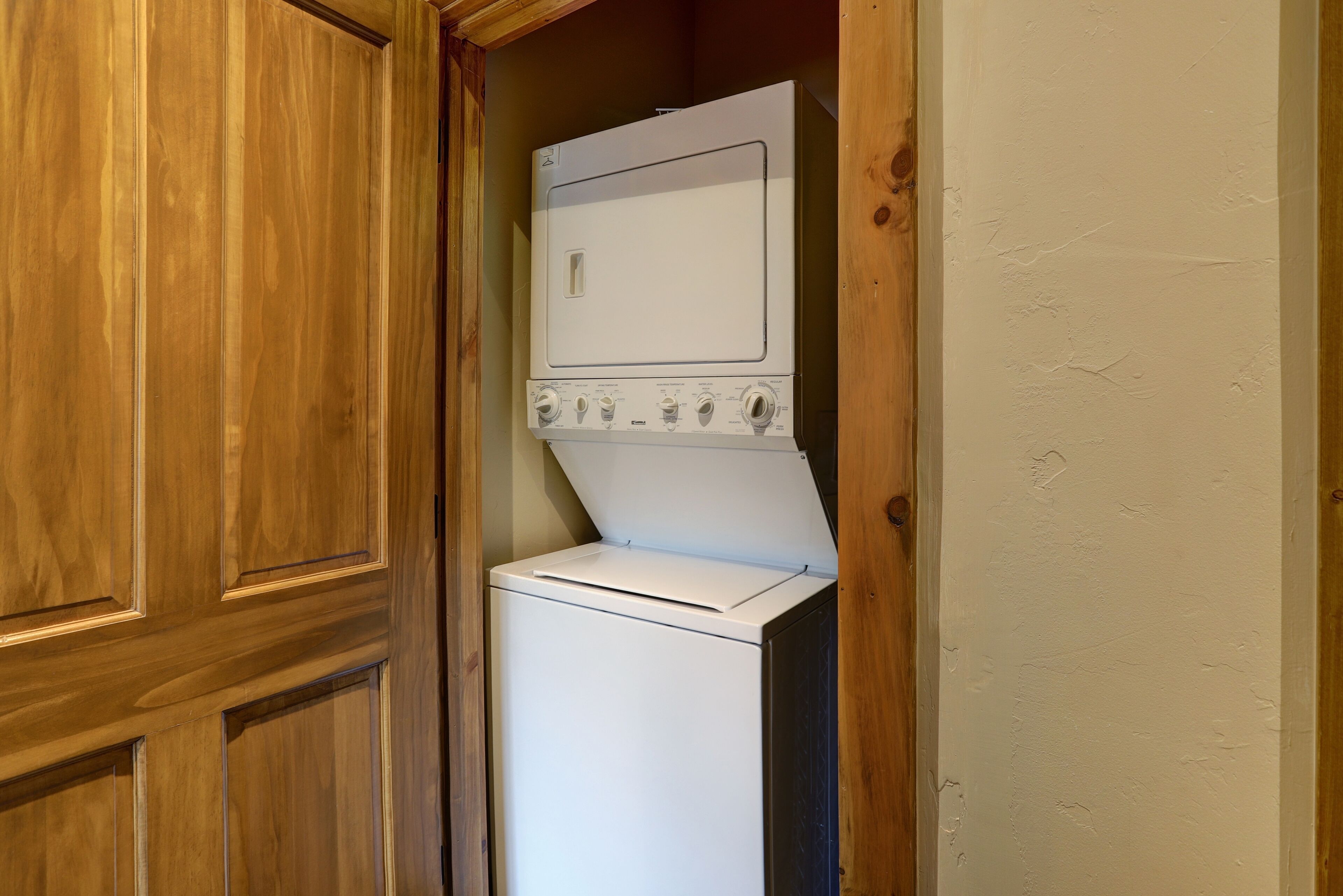 A compact laundry room with a washer and dryer, wooden cabinetry, and a plain wall.