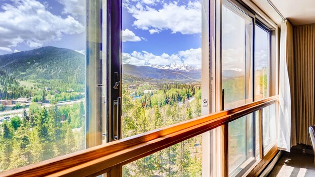 Una habitación con amplios ventanales que ofrecen vistas a un paisaje montañoso con picos nevados y un valle boscoso.
