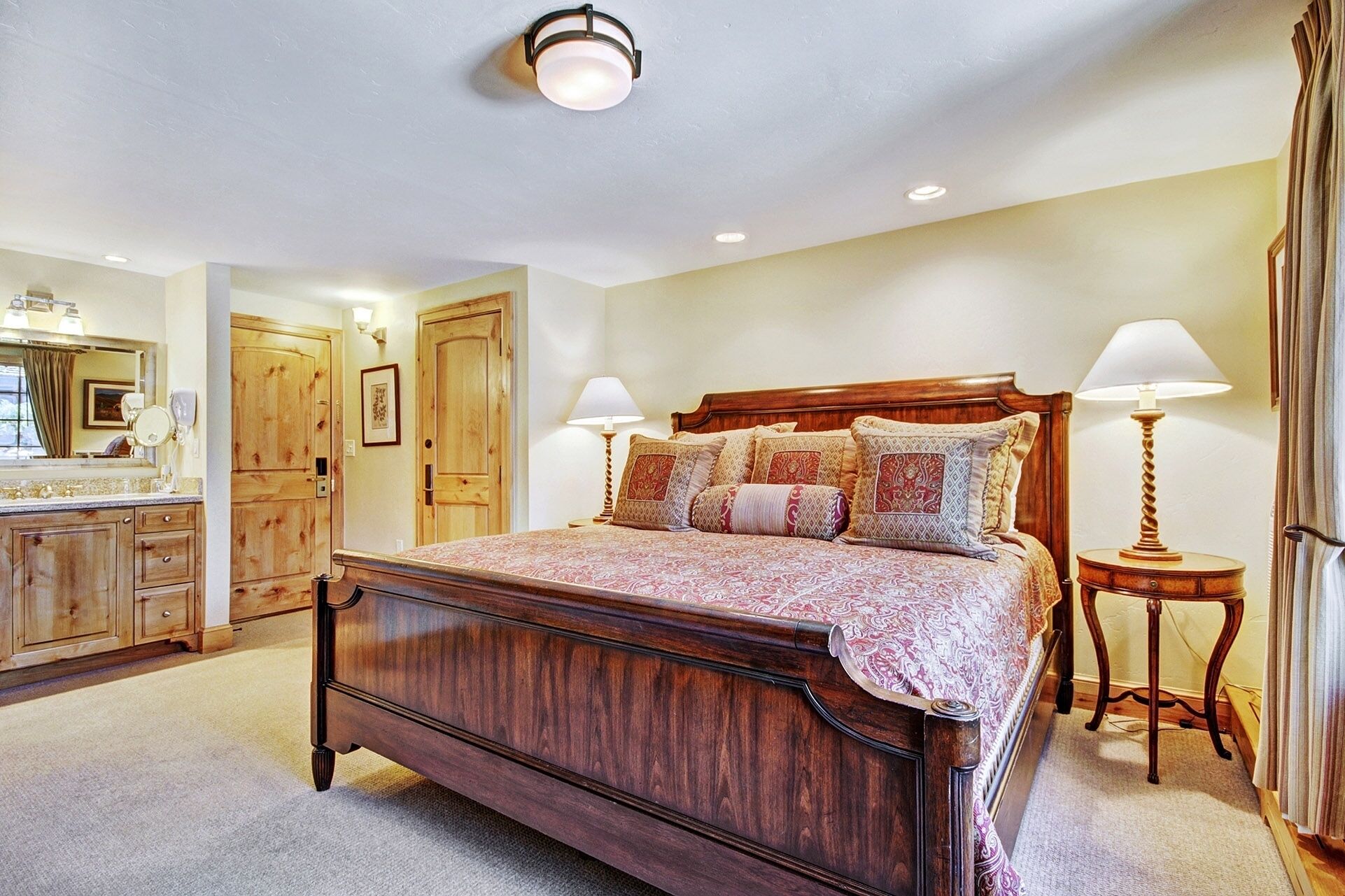 A bedroom with a wooden bed, two bedside lamps, a wooden nightstand, a mirror, and a door.