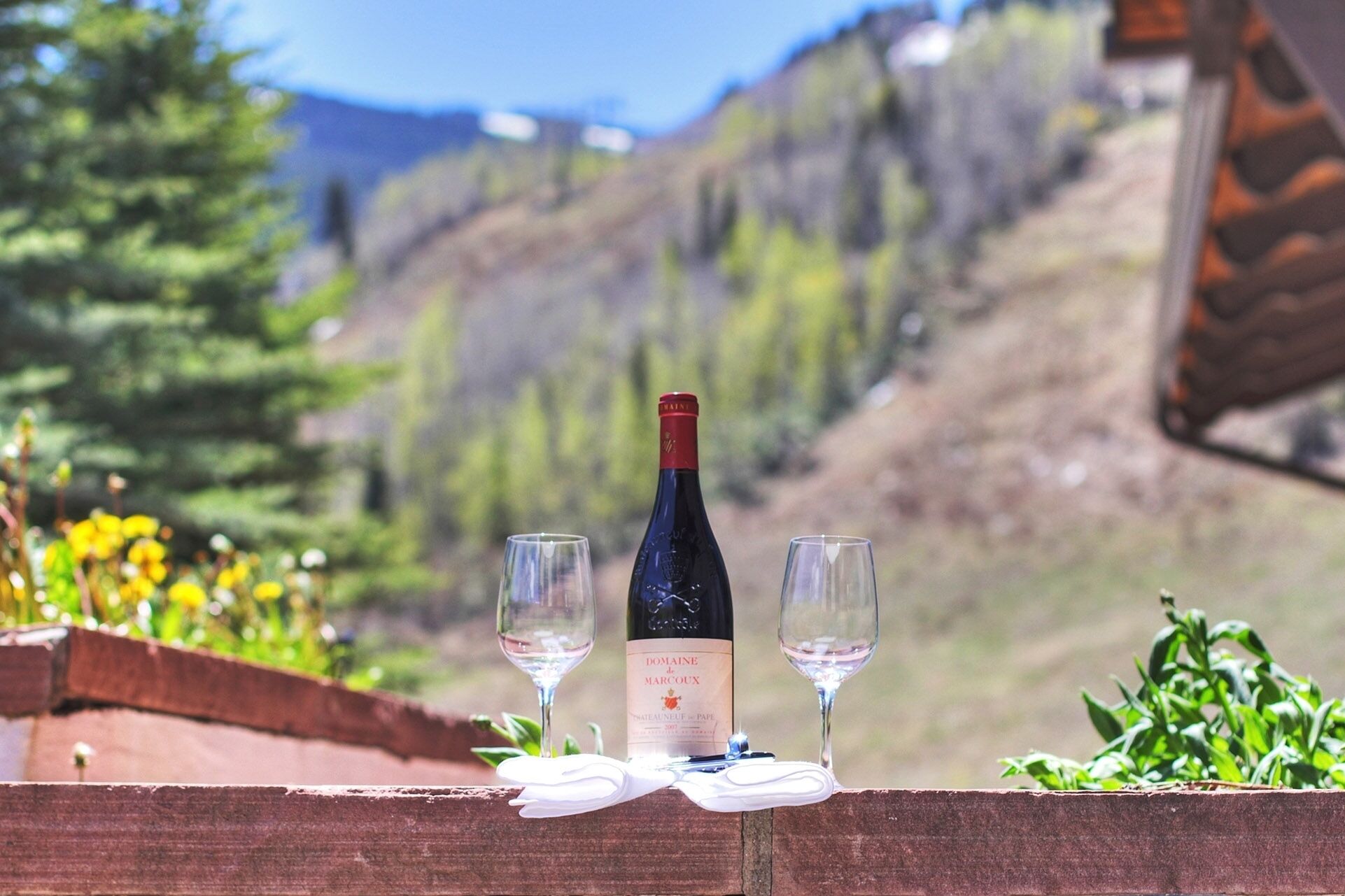 A bottle of Domaine de Marcoux wine and two glasses on a wooden ledge with a mountainous backdrop.