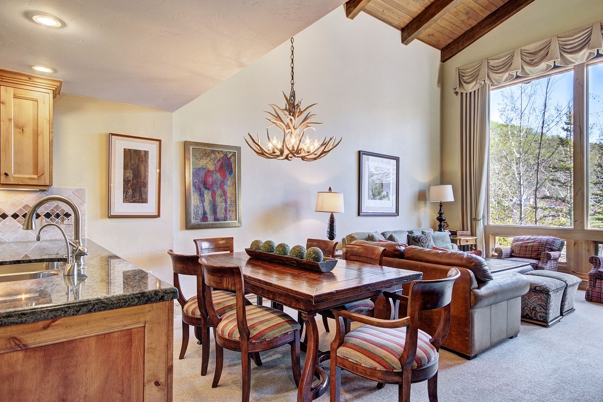 A spacious living area with a dining table, chairs, and a sofa. There is a chandelier hanging from the ceiling, and artwork on the walls.