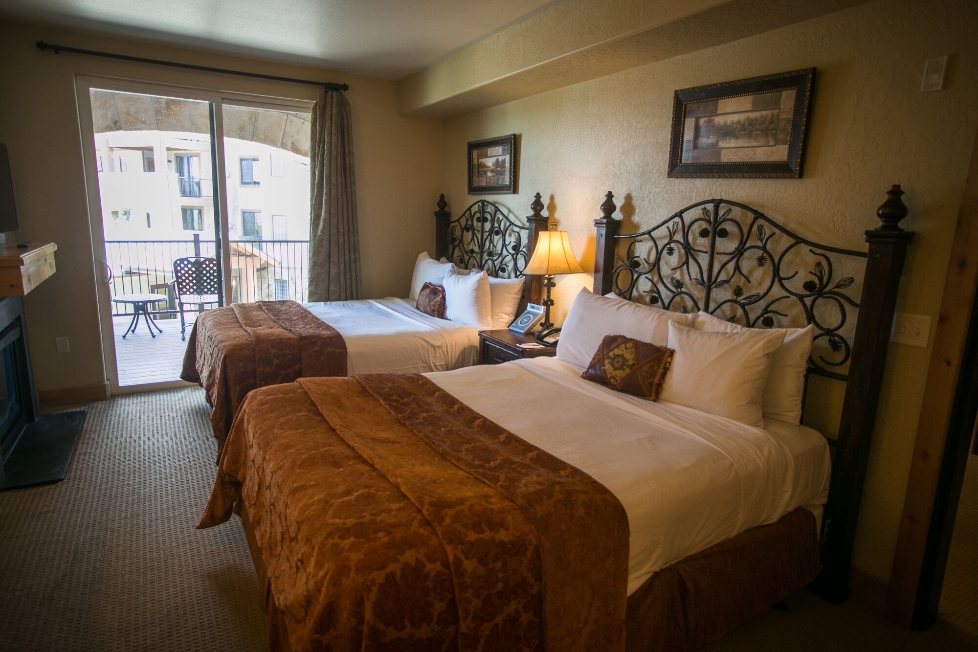 A hotel room with two beds, a balcony, and a view of buildings.