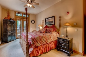 A bedroom with a four-poster bed, a wooden dresser, a lamp, and a painting on the wall. - Luxury 3br Ski In-out /firepit, Pool, Sauna 3 Bedroom Condo by RedAwning (Keystone)