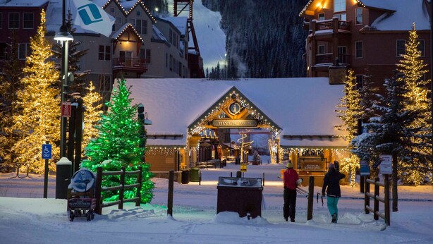 Ein verschneites Dorf mit beleuchteten Gebäuden und einem Weihnachtsbaum.