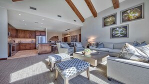 A spacious living area with a kitchen in the background, a dining area, and a seating area with a sofa and ottomans.
