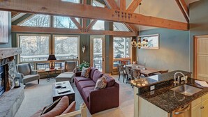 A spacious living area with a fireplace, large windows, and a kitchen with granite countertops. - Slopeside Living - 3br 4ba At Pines Lodge 3 Bedroom Condo by RedAwning (Avon)