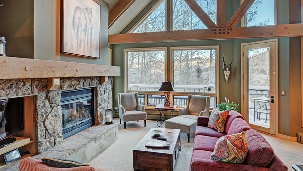 A spacious living room with a stone fireplace, comfortable seating, and large windows offering a view of the outdoors. - Slopeside Living - 3br 4ba At Pines Lodge 3 Bedroom Condo by RedAwning (Avon)