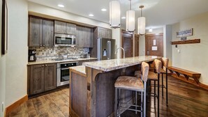 A modern kitchen with wooden cabinets, stainless steel appliances, a large island with bar stools, and pendant lighting. - Luxury  At Base Of Peak 8, Steps From Winter Activities 2 Bedroom Condo by RedAwning (Breckenridge)