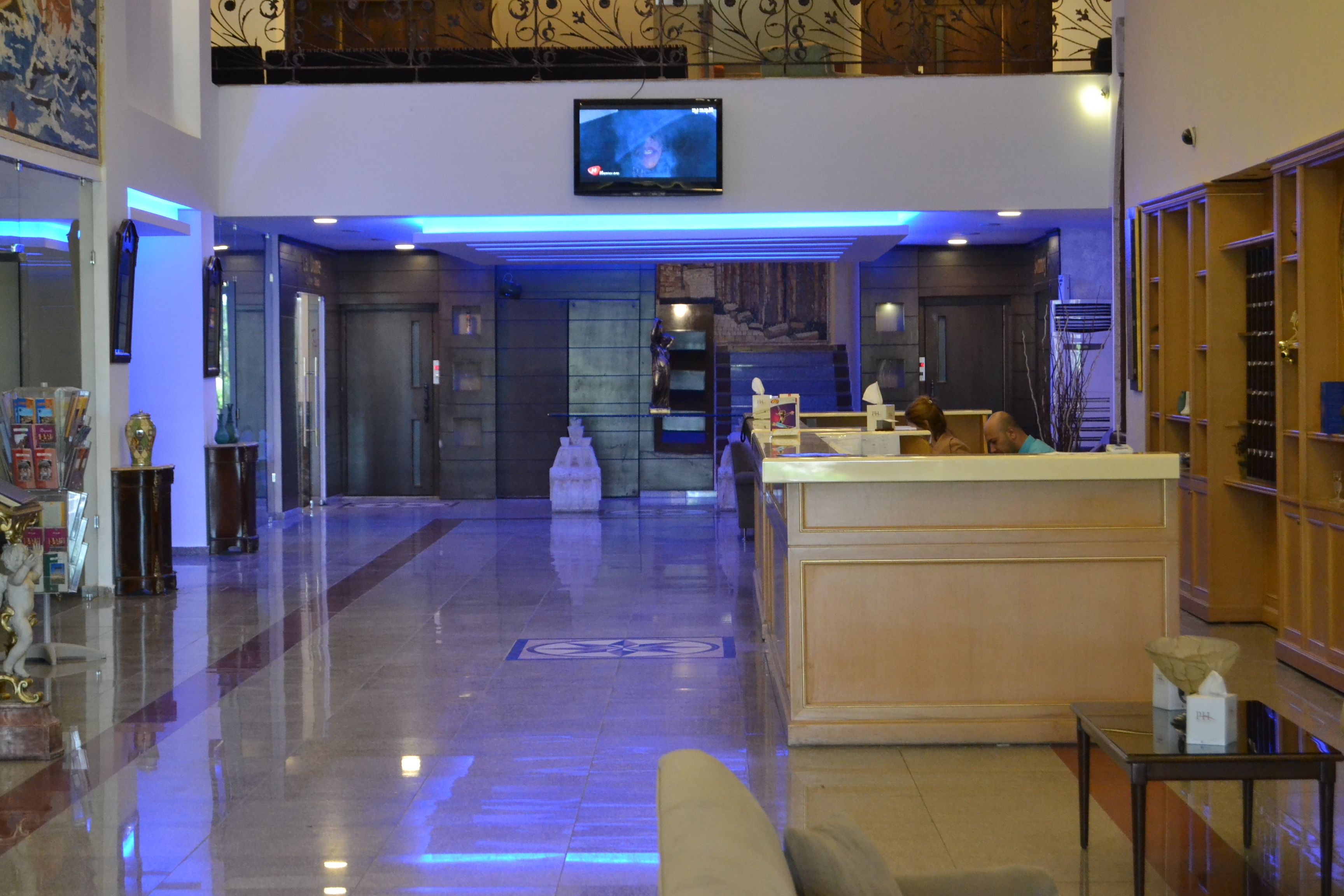 A hotel lobby with a reception desk, a television mounted on the wall, and a polished marble floor.