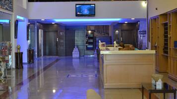 A hotel lobby with a reception desk, a television mounted on the wall, and a polished marble floor.