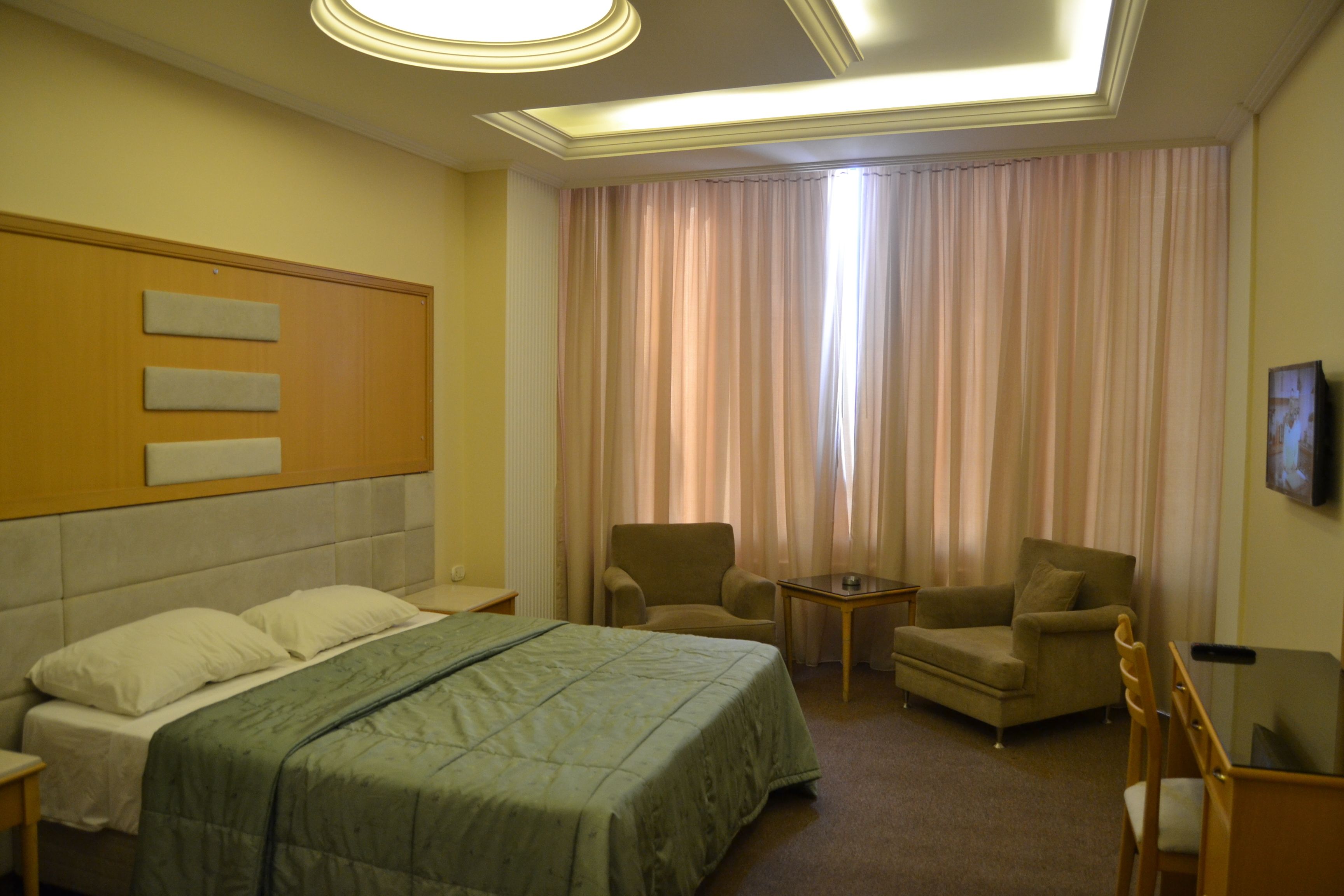 A hotel room with a bed, two armchairs, a small table, and a television.