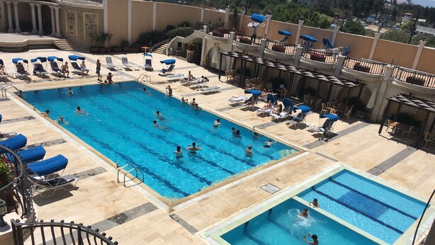 Un área de piscina en la azotea con múltiples piscinas, tumbonas y una escalera que conduce a un nivel superior.
