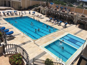 Un área de piscina en la azotea con múltiples piscinas, tumbonas y una escalera que conduce a un nivel superior.