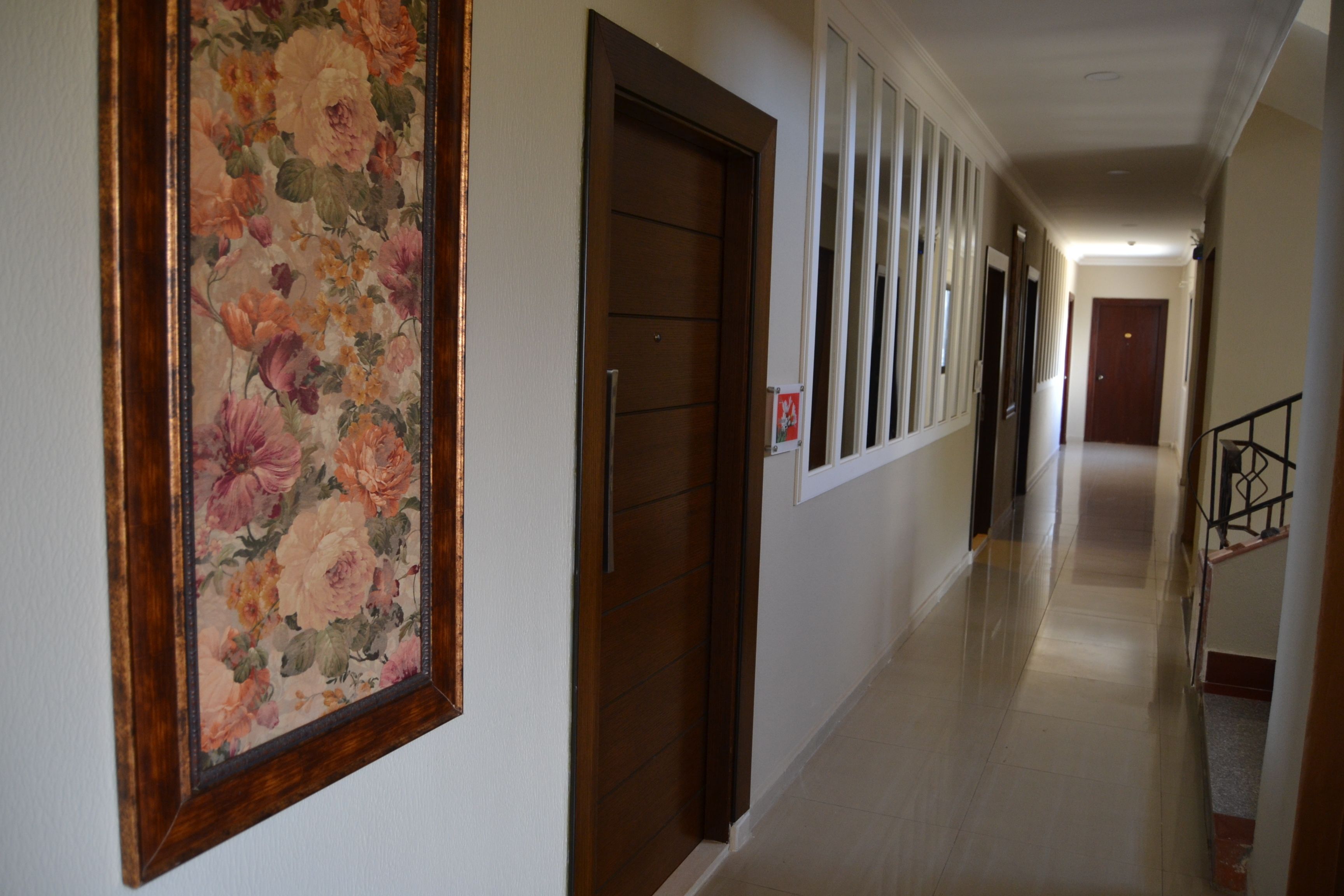 Un pasillo con un cuadro floral, una puerta de madera y una escalera con barandilla de metal.