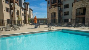 A swimming pool with lounge chairs and umbrellas, surrounded by multi-story buildings with balconies. - Stay in Comfort while Enjoying Valley Views by RedAwning (Park City)