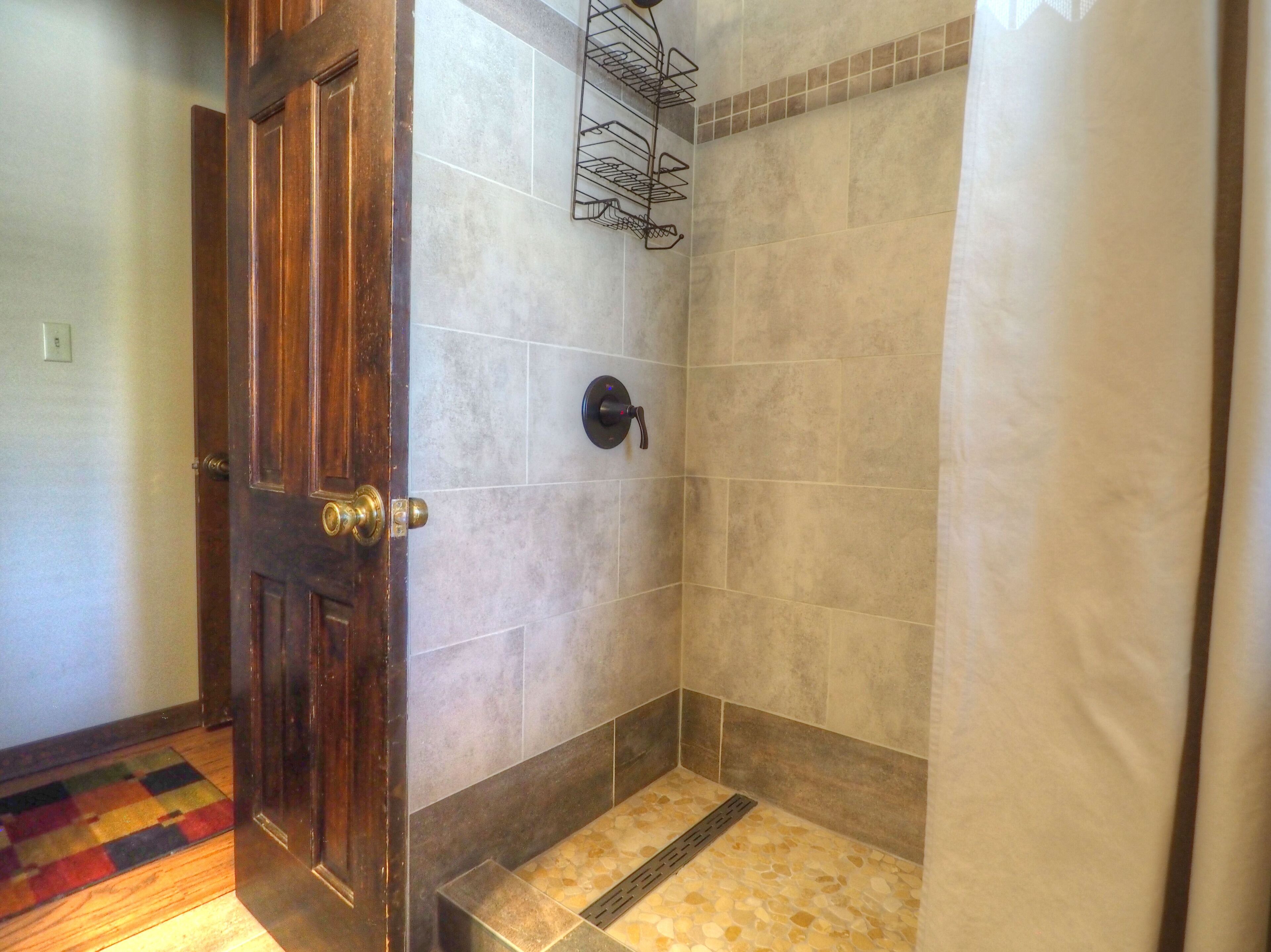 Un espacio de ducha con paredes de azulejos, una puerta de madera y un perchero metálico.
