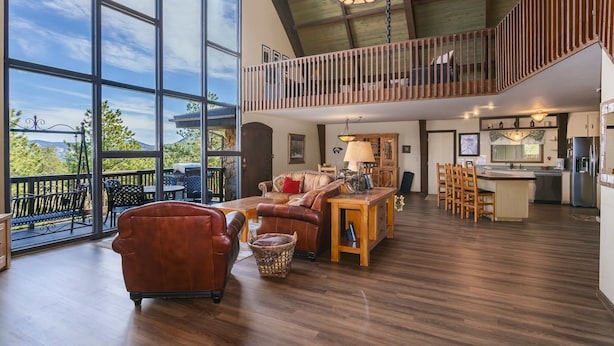 A spacious living area with a large window, a wooden dining table, and a kitchen area. - Sky View In The Rockies -- Ev #3473 3 Bedroom Home by RedAwning (Estes Park)