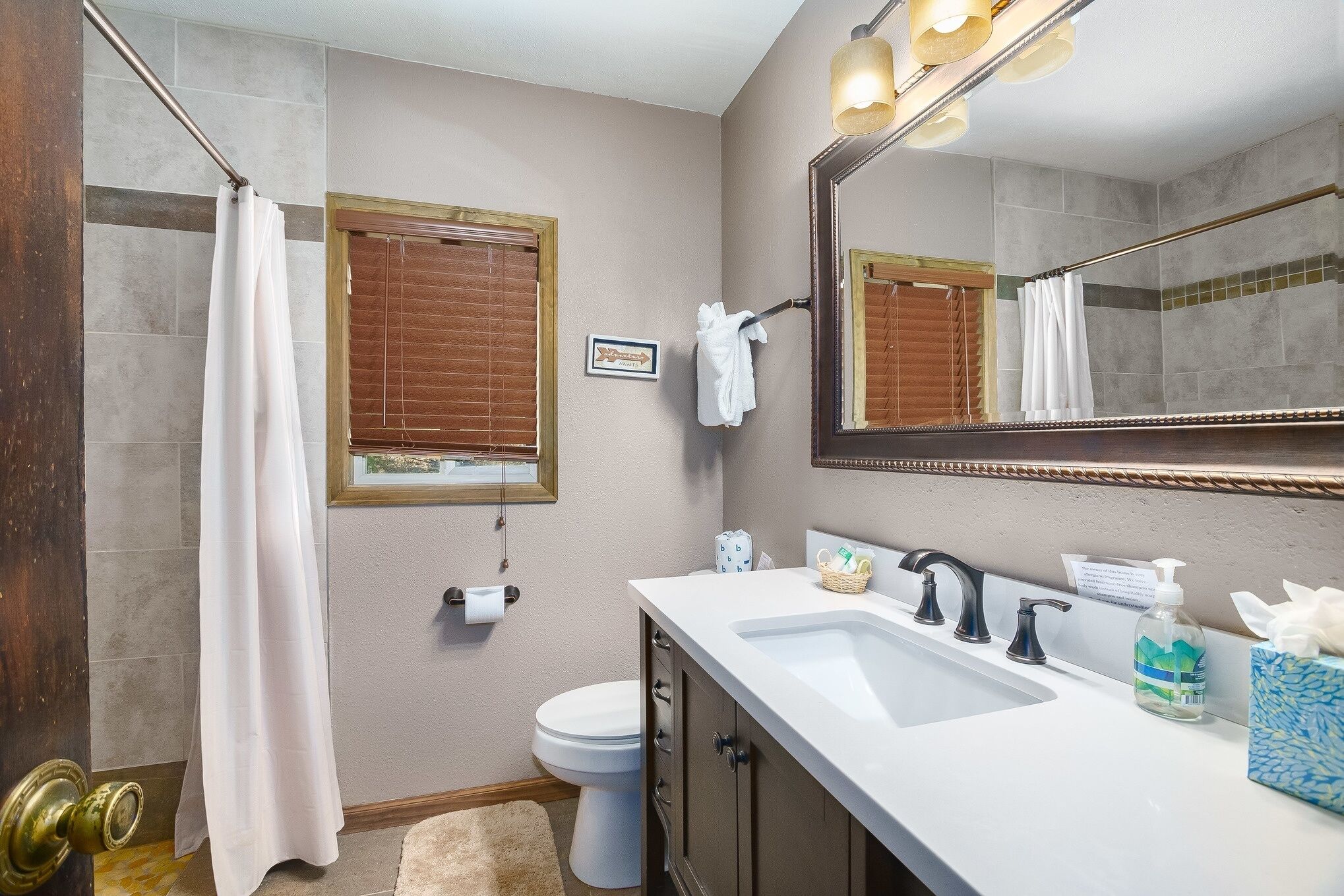 A bathroom with a shower, toilet, sink, and a large mirror.