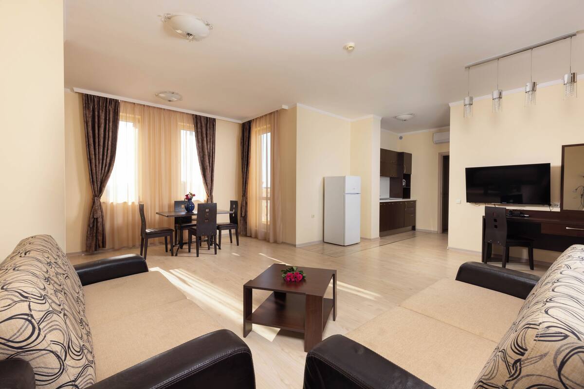 Una sala de estar moderna con un sofá, una mesa de centro, un televisor y una cocina al fondo.