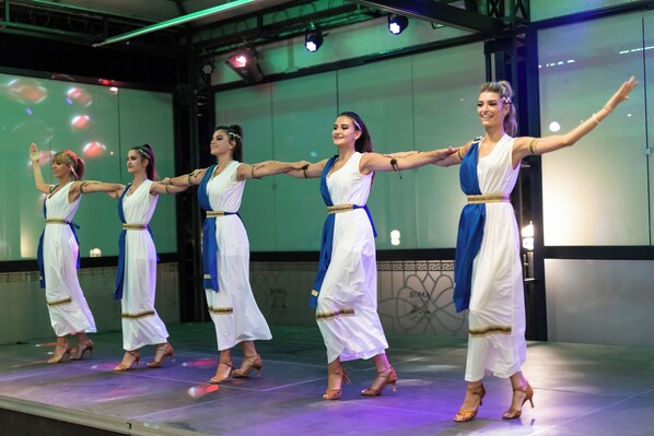 Un grupo de bailarines actuando en un escenario con un fondo que muestra un muro con grafitis y la palabra 'ROMA'.