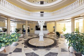 A spacious lobby with a central white statue, multiple floors with balconies, and potted plants. - Rome Palace Deluxe (Sunny Beach)