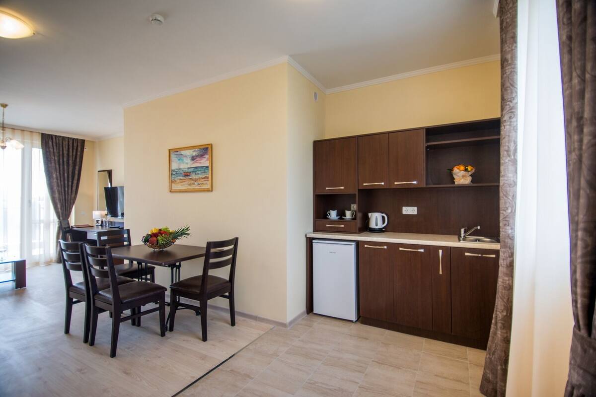 Una cocina compacta con armarios de madera, un refrigerador pequeño y una zona de comedor con una mesa y sillas.