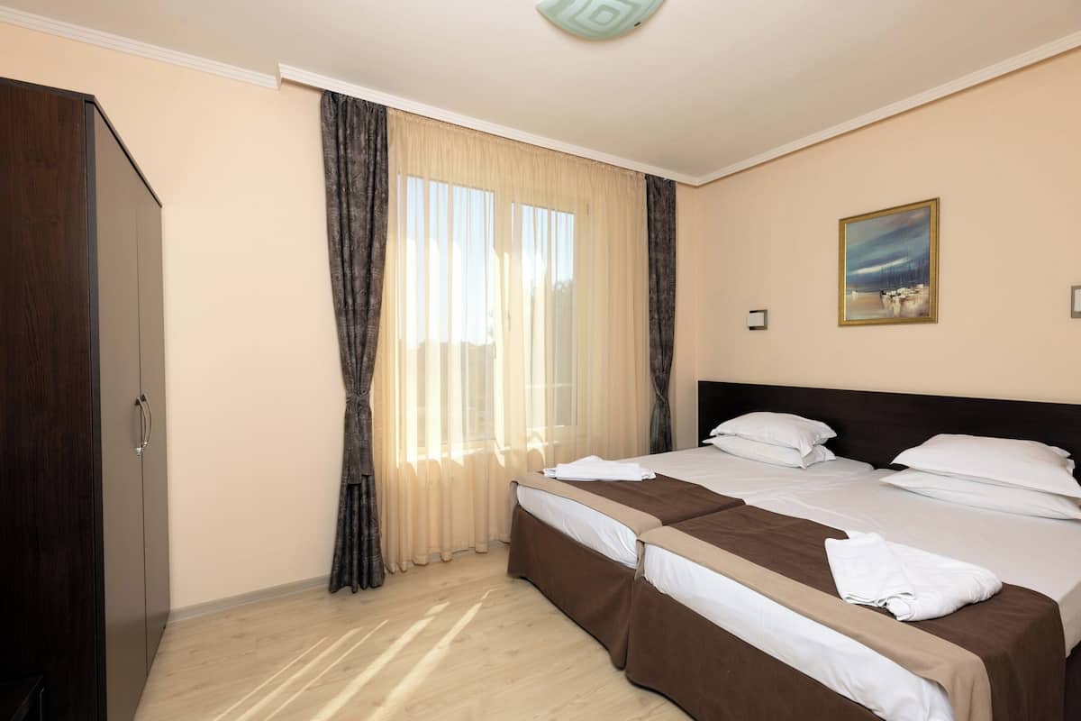 Habitación de hotel con dos camas, un armario, un cuadro en la pared y una ventana con cortinas.
