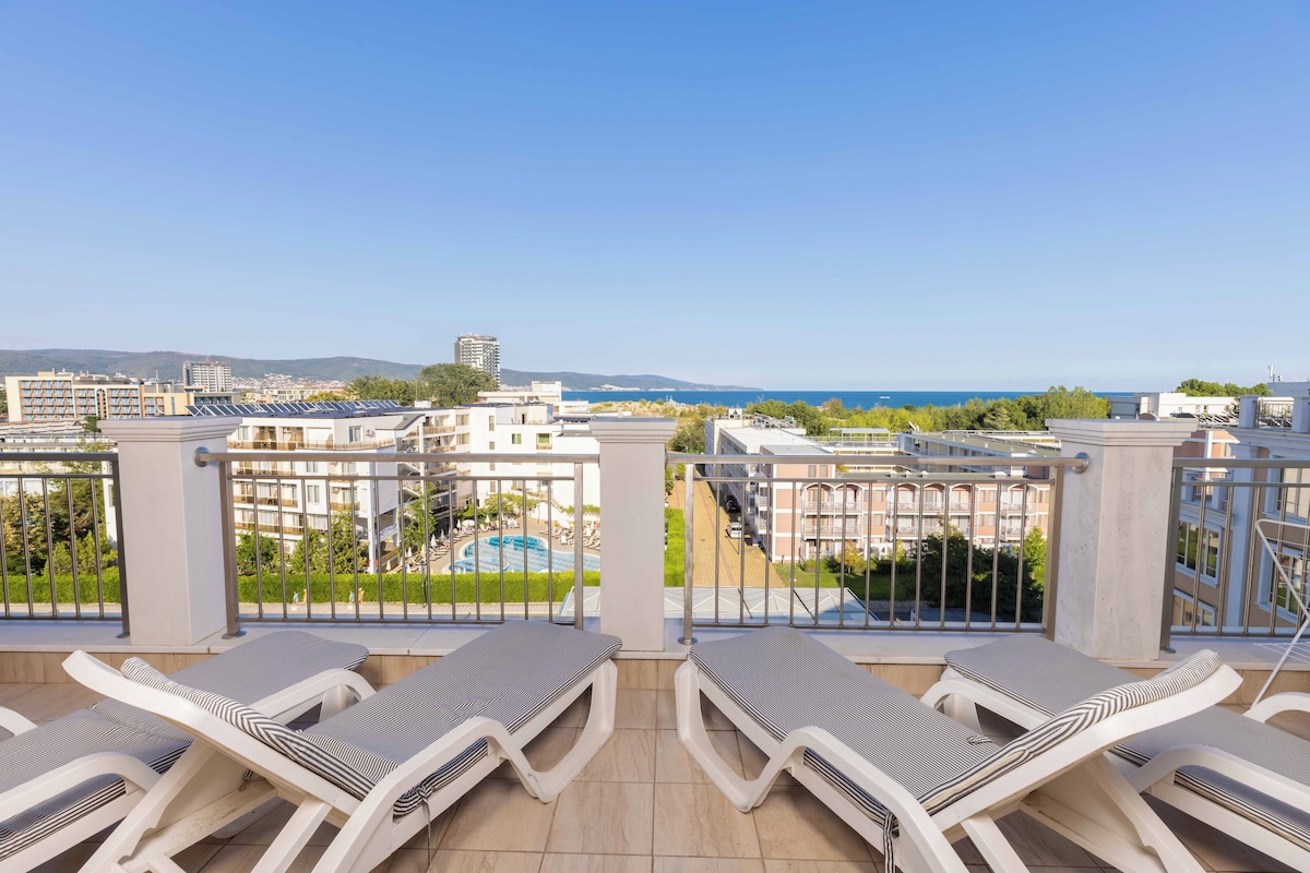 Ein Balkon mit Liegestühlen, Blick auf einen Pool und umliegende Gebäude.
