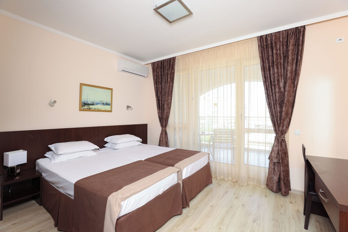 Habitació d'hotel amb dos llits, escriptori, cadira, tauleta de nit i un quadre a la paret.