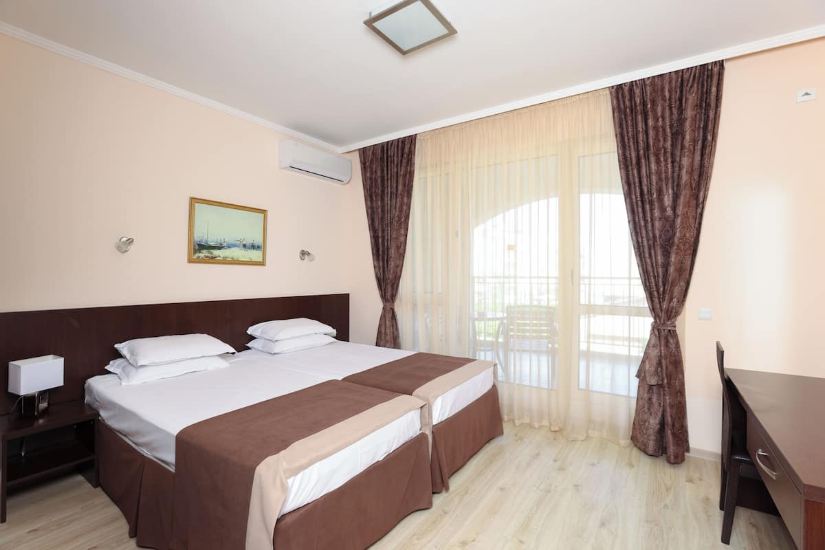 Habitación de hotel con dos camas, un escritorio, una silla, una mesita de noche y un cuadro en la pared.