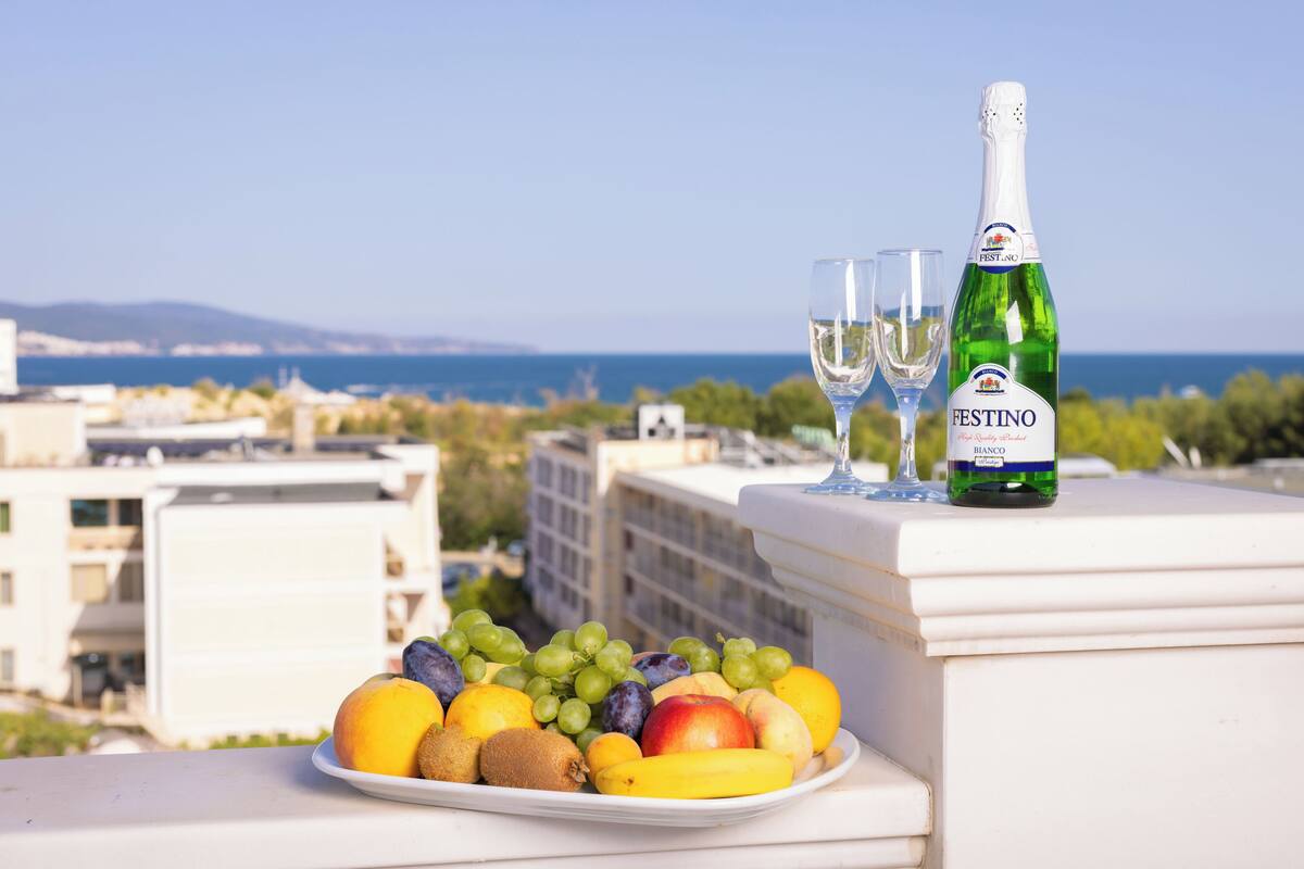 Un plato de fruta y una botella de vino blanco FESTINO en un balcón con vista al mar.