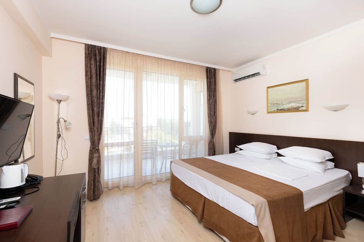 Habitación de hotel con cama, escritorio con computadora, televisión y ventana con cortinas.