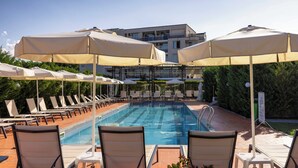 A swimming pool with lounge chairs and umbrellas, surrounded by greenery and a building in the background. - Rome Palace Deluxe (Sunny Beach)