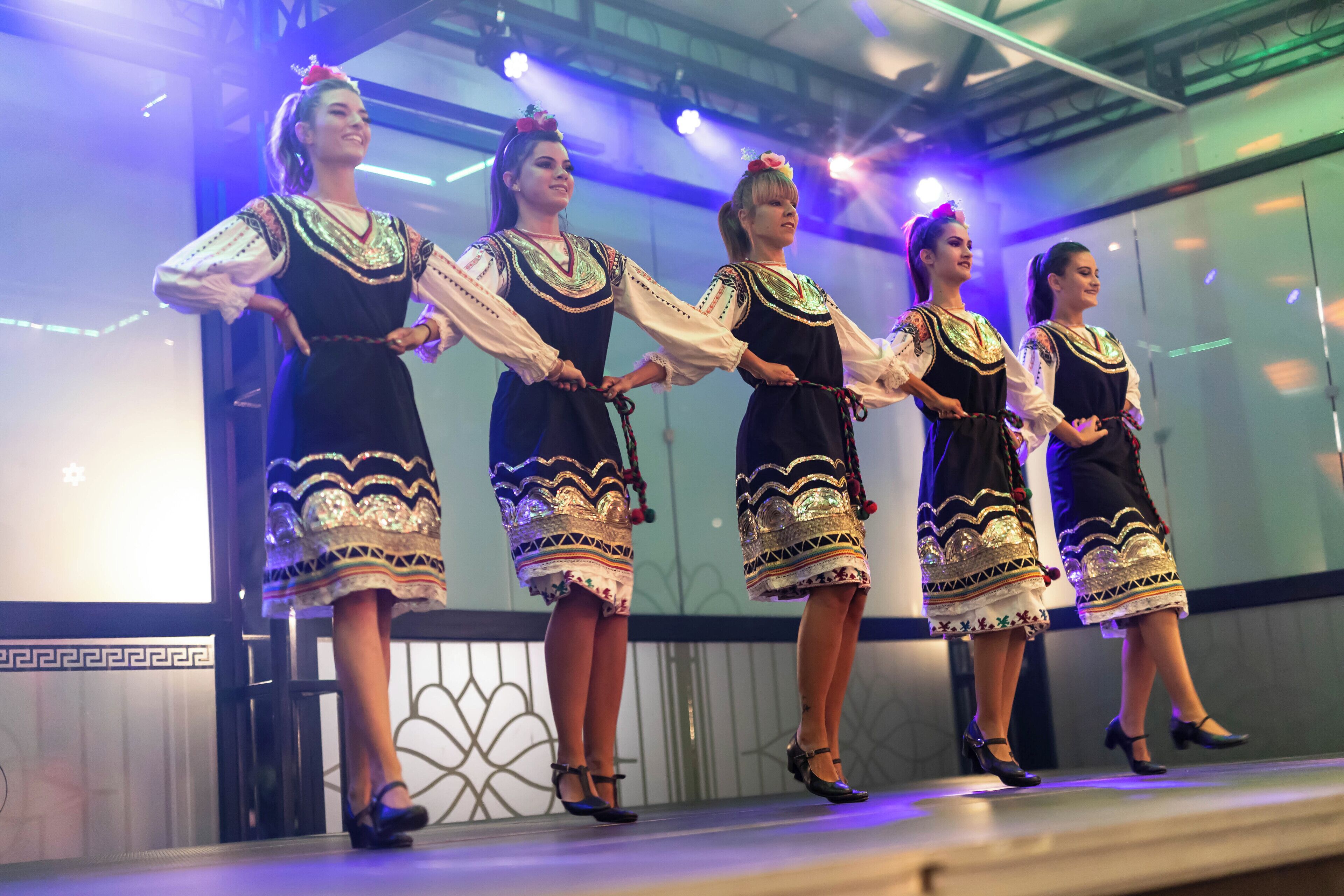Un grupo de personas vestidas con atuendos tradicionales se presenta en un escenario con un fondo moderno.