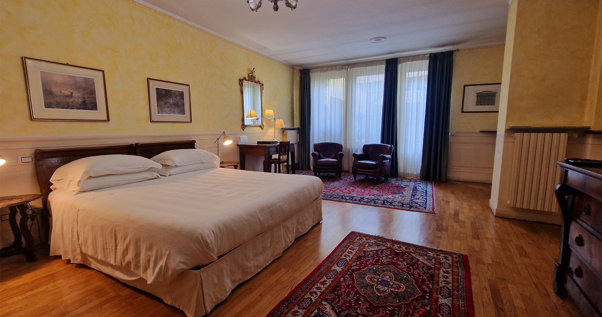 Una habitación de hotel con una cama grande, dos sillas, un escritorio y una ventana con cortinas.