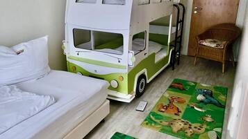 Ein Zimmer mit einem Etagenbett, einem Einzelbett, einem Stuhl und zwei Teppichen mit Tiermotiven.