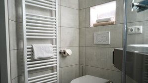 A modern bathroom with a white toilet, a towel rack, and a glass shower enclosure. - LoC - Hotel Kannenkeller Smart Stay (Lauingen)