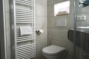 A modern bathroom with a white toilet, a towel rack, and a glass shower enclosure. - LoC - Hotel Kannenkeller Smart Stay (Lauingen)