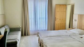 Una camera d'albergo con un letto, una scrivania, una sedia, una finestra con tende e un termosifone.