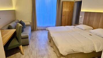 A hotel room with a bed, a sofa, a desk, and a window with curtains.