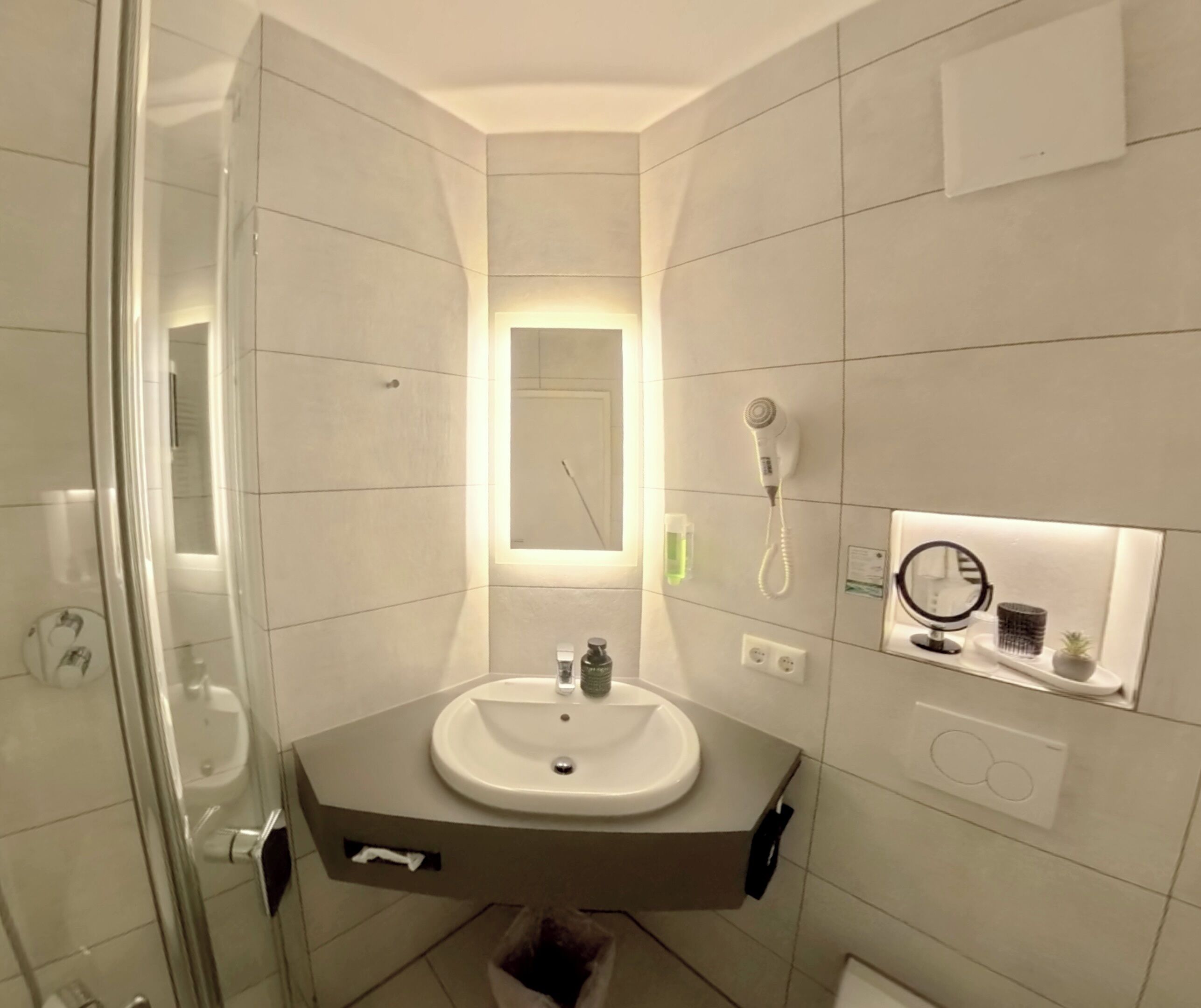 Un baño moderno con cabina de ducha de vidrio, tocador con lavabo y espejo con luz de aro.