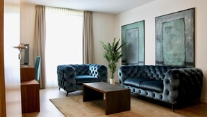A living room with two dark blue tufted sofas, a wooden coffee table, a potted plant, and two abstract paintings on the wall. - LoC - Hotel Kannenkeller Smart Stay (Lauingen)